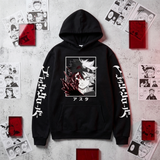 A black pullover hoodie with a large anime character graphic on the chest, white Japanese text printed down both sleeves, and a front kangaroo pocket, displayed on a textured light gray background surrounded by manga-style prints and red boxes.