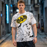 A man wearing a white short-sleeve t-shirt with a black and yellow Batman comic print, standing in a blurred urban alleyway.