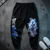 Black Dragon Ball Z sweatpants with blue side piping, featuring a large Blue Spirit character graphic on the right leg and the Dragon Ball Z logo on the left leg, shown in a flat-lay on a concrete floor with white sneakers.