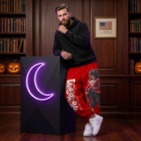 A man leans against a black display pedestal with a glowing purple crescent moon in a dark wood library setting. He is wearing a black hoodie, red graphic sweatpants, and white sneakers.