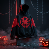 A black and red pullover hoodie with a large red spider emblem on the chest, displayed on a dark metal stand in a Halloween-themed setting with glowing jack-o'-lanterns and hanging chains.