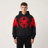 A man wearing a black and red pullover hoodie with a large red spider emblem on the chest, paired with black pants, against a plain light gray background.