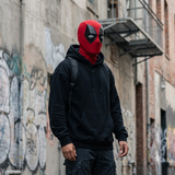A person wearing a red and black Deadpool mask, a black hoodie, and dark cargo pants standing in an urban alleyway with graffiti-covered walls.
