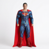 Superman action figure or collectible statue in a full-body pose, wearing a textured blue suit with a red cape and boots, standing against a plain light gray studio background.