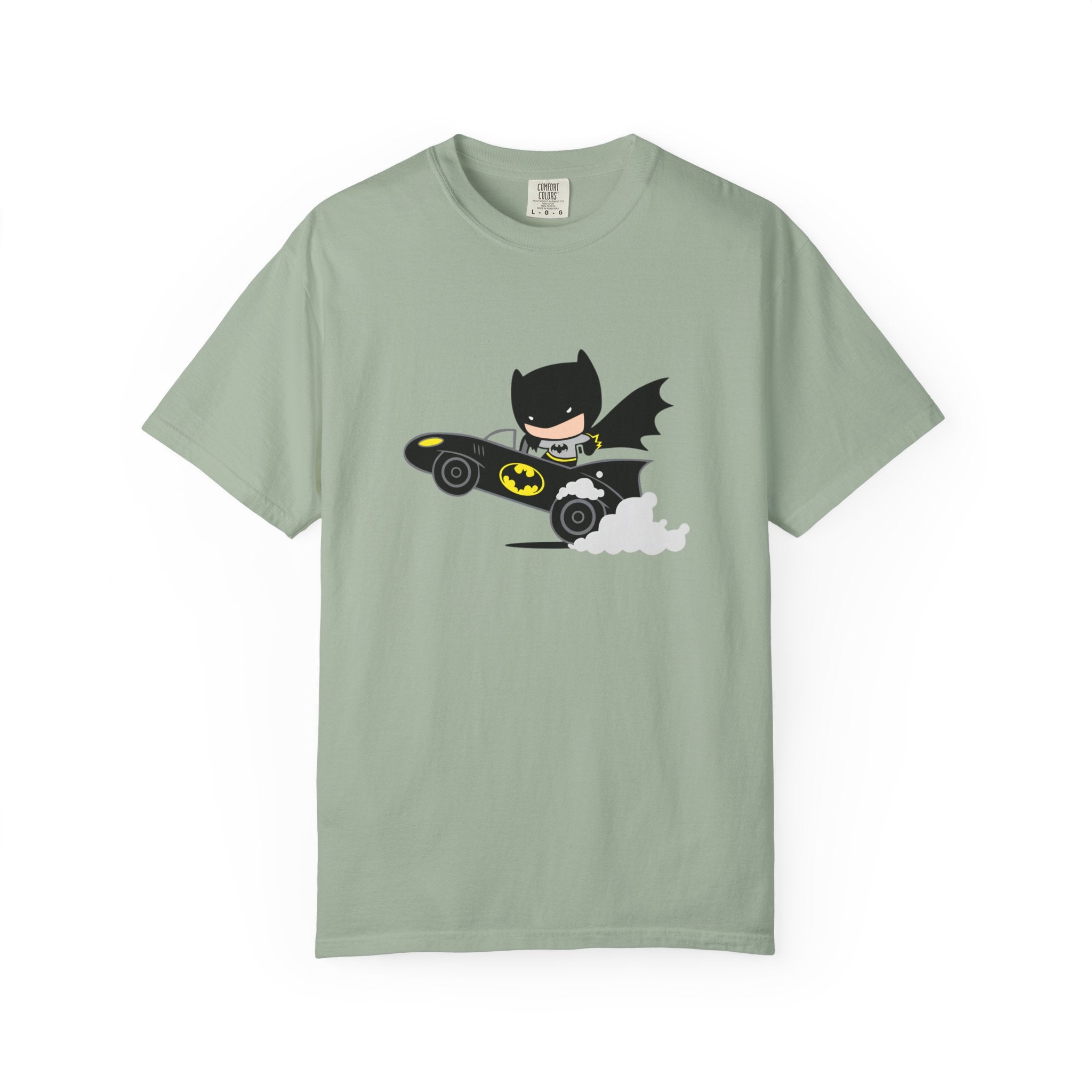 A sage green short-sleeve crewneck t-shirt featuring a cartoon graphic of Batman driving a black Batmobile with yellow accents and white smoke, displayed on a clean white background.