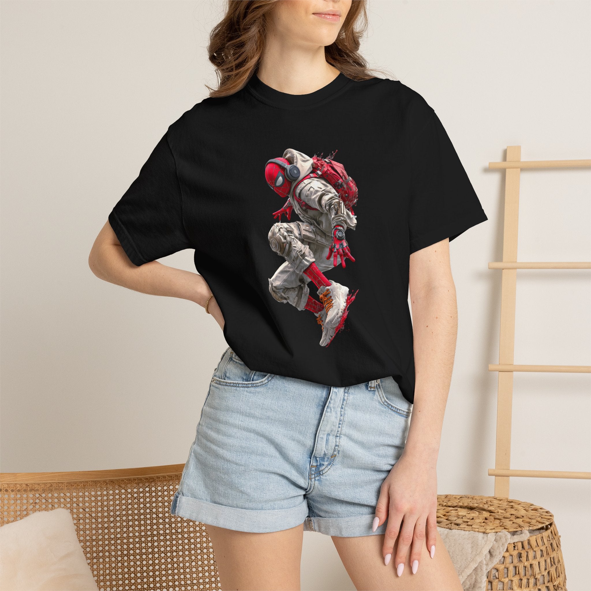 A woman wearing a black short-sleeve graphic t-shirt with a detailed print of a crouching astronaut in red, white, and gray, paired with light-wash denim shorts in a neutral indoor setting.