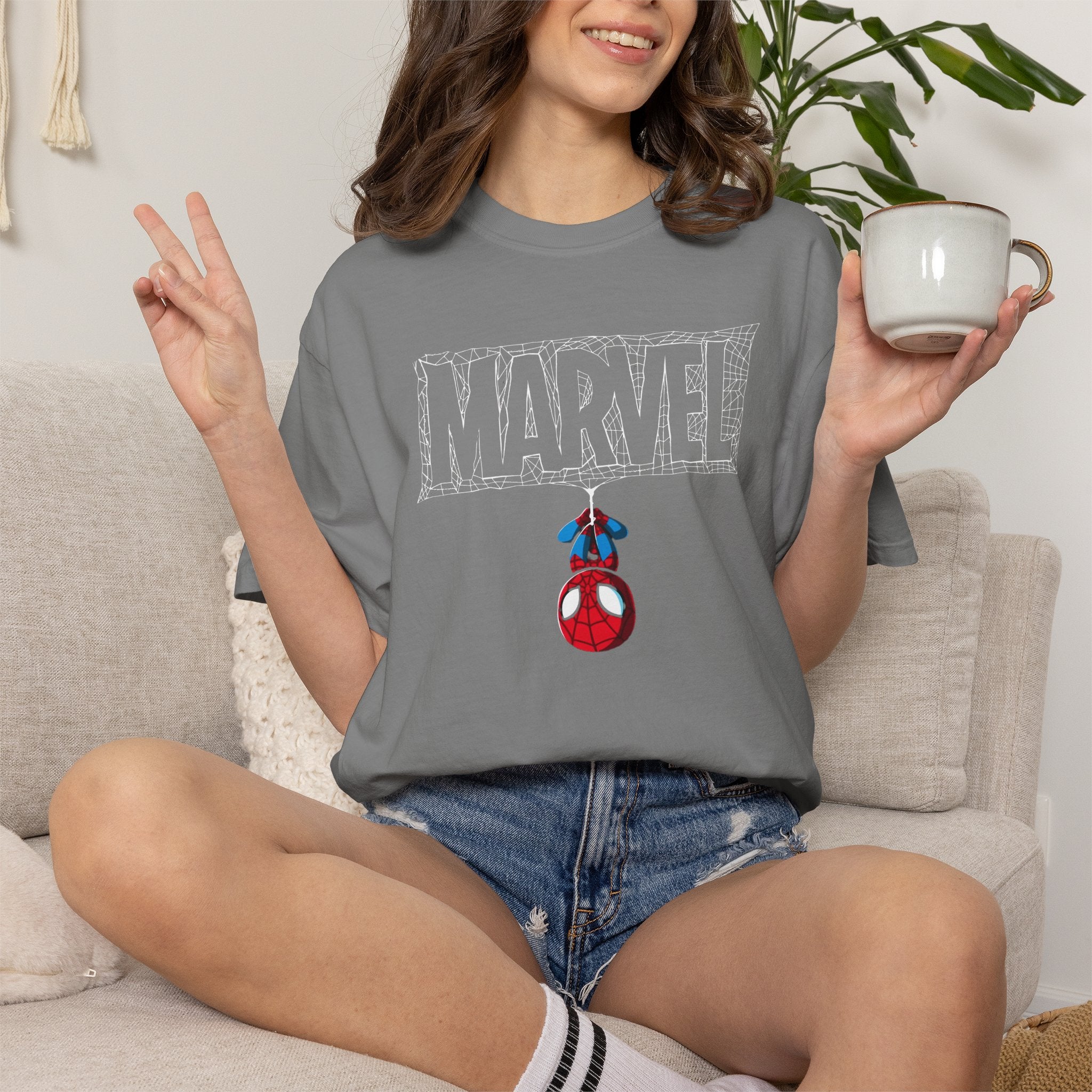Person wearing a gray t-shirt with 'MAMA' printed in floral letters, sitting on a couch holding a mug.