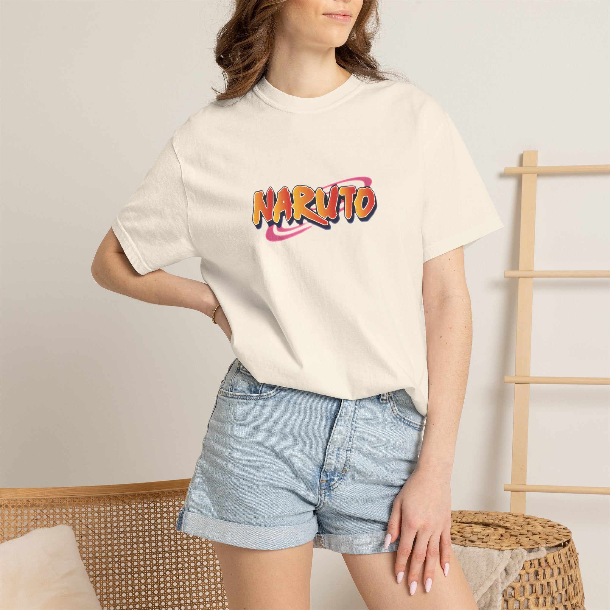 A woman wearing a cream-colored t-shirt with a colorful 'NARUTO' graphic on the chest, paired with light-wash denim shorts, standing in a brightly lit room.