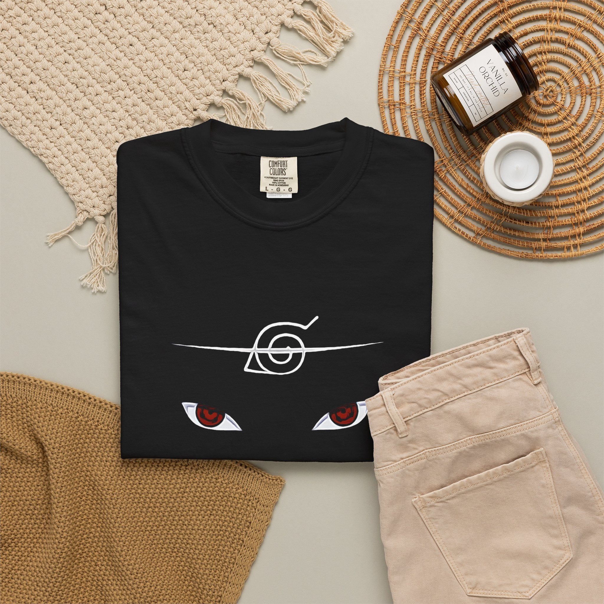 A folded black T-shirt with a white 'HT' monogram and the text 'HER TAKEOVER' and 'THE NIGHT BELONGS TO YOU' is styled in a flat lay with beige pants, a woven blanket, a candle jar, and a small cup on a neutral background.