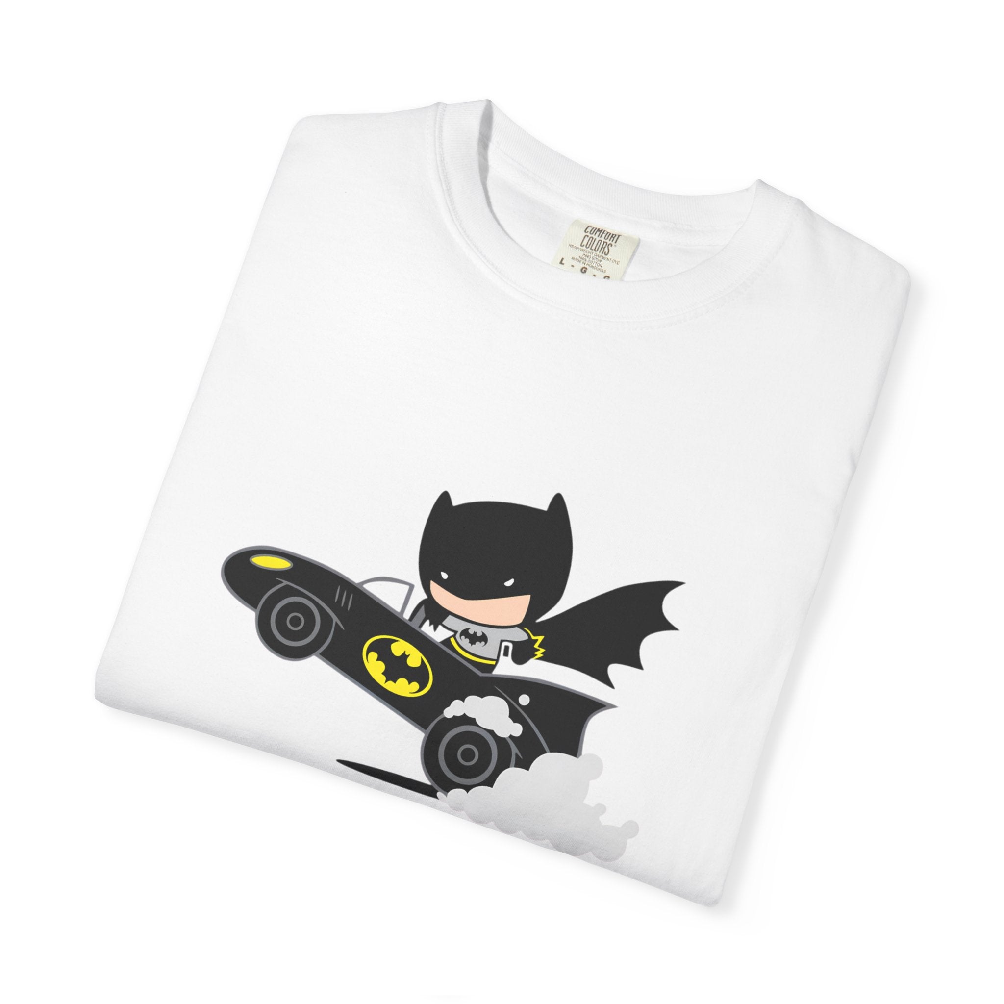 A folded white crewneck t-shirt featuring a cartoon graphic of Batman riding his black Bat-Bat car with yellow accents and gray smoke details, set against a plain white background.