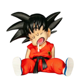 A collectible figurine of Goku from Dragon Ball Z, shown sitting down with his mouth open in a yawn or gagging expression. He is wearing his iconic orange gi with a black belt and has spiky black hair.