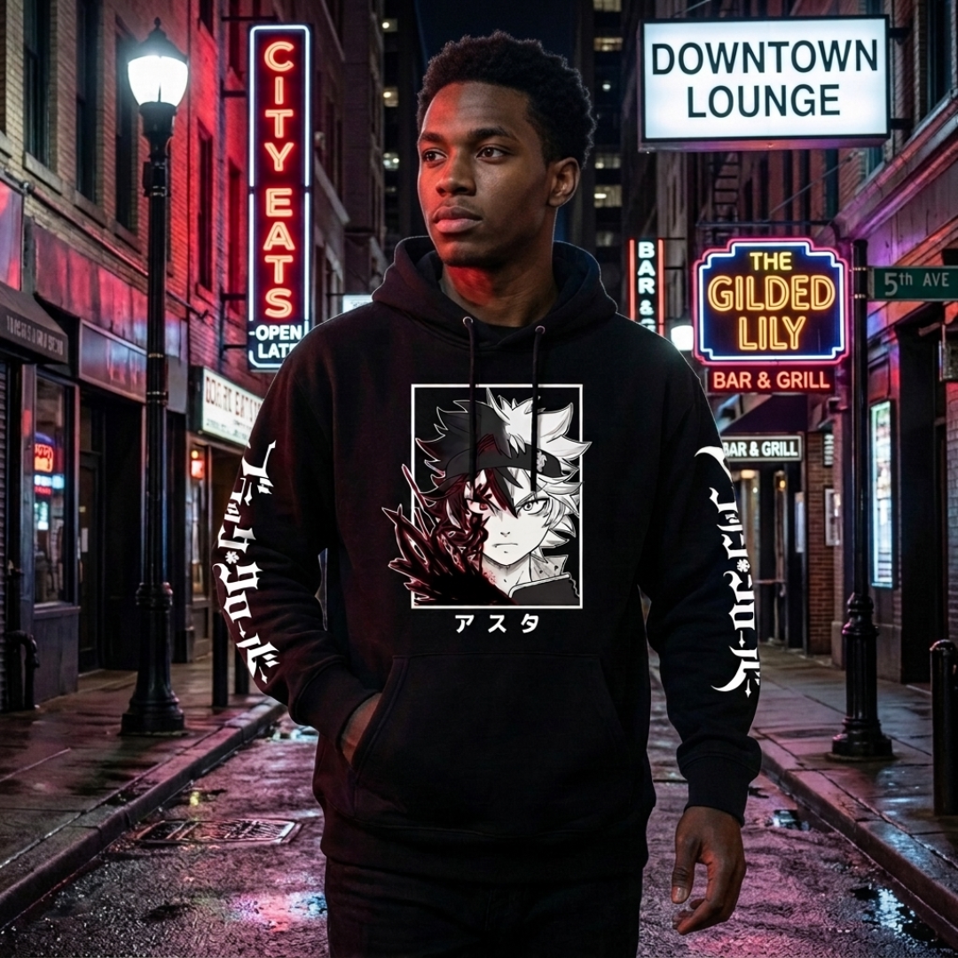 A man wearing a black pullover hoodie with a large anime-style graphic on the chest and white text down the sleeves, standing on a wet city street at night with neon signs in the background.