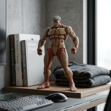 A muscular male action figure with exposed anatomical muscle details stands on a desk beside books, folded gray sweatshirts, and a keyboard in a modern indoor setting.