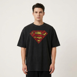 A man wearing a black t-shirt with a distressed red and yellow Superman logo on the chest, standing against a light gray background.