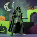 A Doctor Doom action figure posed with one arm raised, wearing a dark green hooded cape and metallic silver armor, set against a Halloween-themed backdrop with pumpkins, a moon, and geometric shapes.