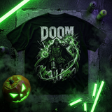 A black graphic t-shirt featuring the word 'DOOM' in distressed white letters above a green and black illustrated character, displayed on a dark textured background with neon green lighting, a carved pumpkin, and spray paint cans.