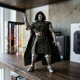 A collectible action figure of Doctor Strange standing on a wooden shelf, wearing his signature dark green cloak and metallic silver armor, with books and a concrete wall in the background.