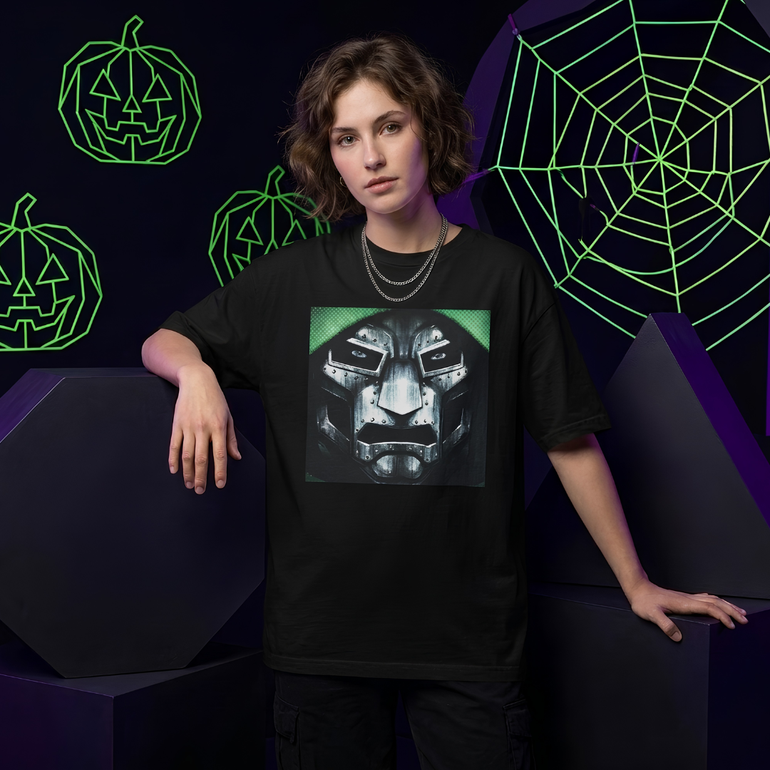A model wearing a black graphic t-shirt featuring a metallic robot face design with green accents, posed against a dark background with neon green pumpkin and spiderweb graphics.