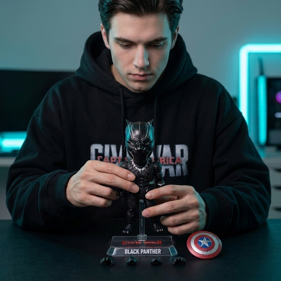 A man in a black hoodie holds a Black Panther collectible figure on a display stand, with a Captain America shield and small accessories on the table in front of him.
