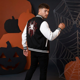 A man wearing a black and white varsity jacket with a red and white spider graphic on the back, posed against a Halloween-themed backdrop with pumpkins and spiderwebs.