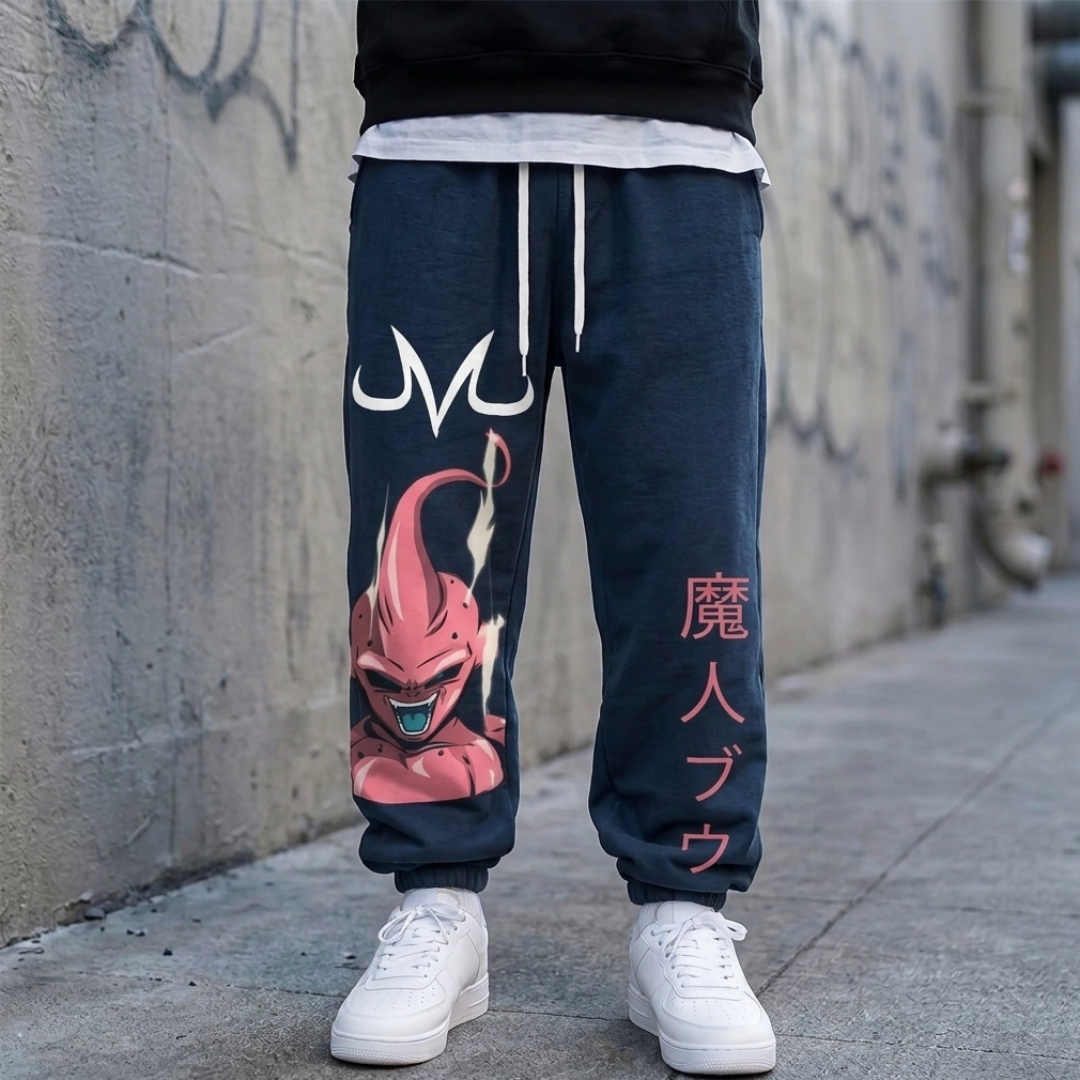 A person wearing dark navy blue sweatpants with a large pink Dragon Ball graphic on the left leg and vertical pink Japanese text on the right leg, paired with white sneakers and a black hoodie, standing against a concrete wall.