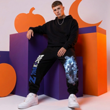 A young man wearing a black hoodie and black sweatpants with graphic prints, sitting on purple and orange geometric blocks.