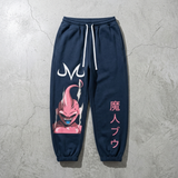 Navy blue sweatpants featuring a pink Dragon Ball graphic on the left leg and pink Japanese characters on the right leg, laid flat on a textured gray concrete background.