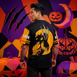 A man wearing a black and yellow short-sleeve t-shirt with a Wolverine graphic on the back, posed in a Halloween-themed setting with geometric pumpkins and a purple background.