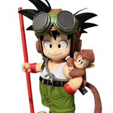 A stylized collectible figure of a cartoon boy with goggles and a red staff, holding a small brown monkey on his shoulder, shown against a plain white background.