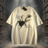An oversized cream-colored t-shirt featuring a black spider graphic and gothic text, presented against a dark, atmospheric background of bookshelves.