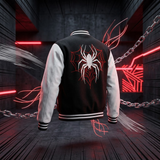 A varsity-style bomber jacket shown from the back, floating in a dark industrial setting with red neon lights and chains. The jacket has a black body with white sleeves and a large white spider over a red web graphic on the back.