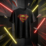 A black washed graphic t-shirt featuring a distressed red and yellow Superman logo on the chest, displayed against a dark concrete background with dramatic red and yellow neon light effects.