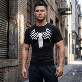 A muscular man wearing a black short-sleeve athletic compression shirt with a large white spider logo on the chest, standing in an urban alleyway.