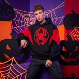 A man wearing a black and red hoodie with a large red spider logo on the chest, posed against a Halloween-themed backdrop with orange web graphics, jack-o'-lanterns, and a purple background.