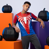 A man modeling a Spider-Man themed short-sleeve t-shirt with a large red and white spider logo on the chest, posed in front of orange and purple geometric blocks with black decorative pumpkins.